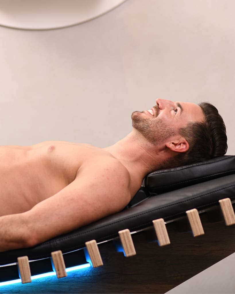 Entspannter Mann liegt auf einer BodyFormer-Liege während einer Anwendung zur Regeneration und Körperformung.