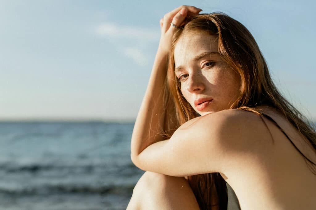 Junge Frau sitzt am Meer in der Sonne und genießt die wohltuende Wirkung des natürlichen Tageslichts.