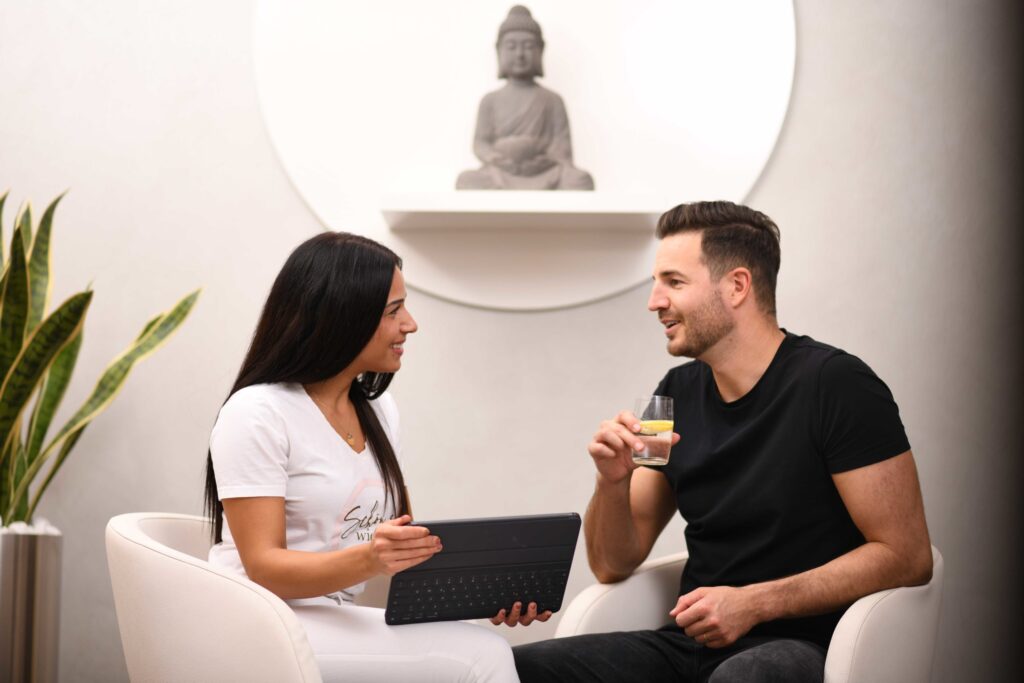 Mitarbeiterin berät einen Kunden in entspannter Atmosphäre zu Gesundheits- und Wellnessangeboten.